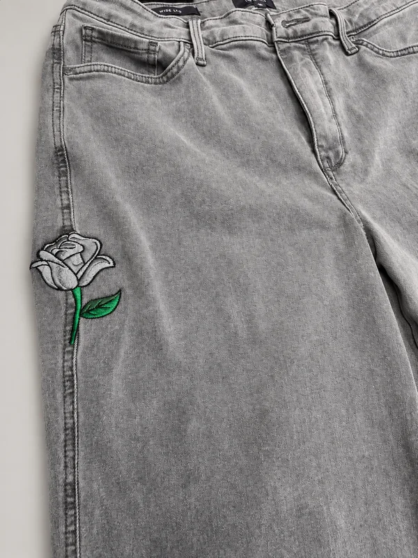 Gray jeans with a gray and green embroidered rose covering a repaired hole