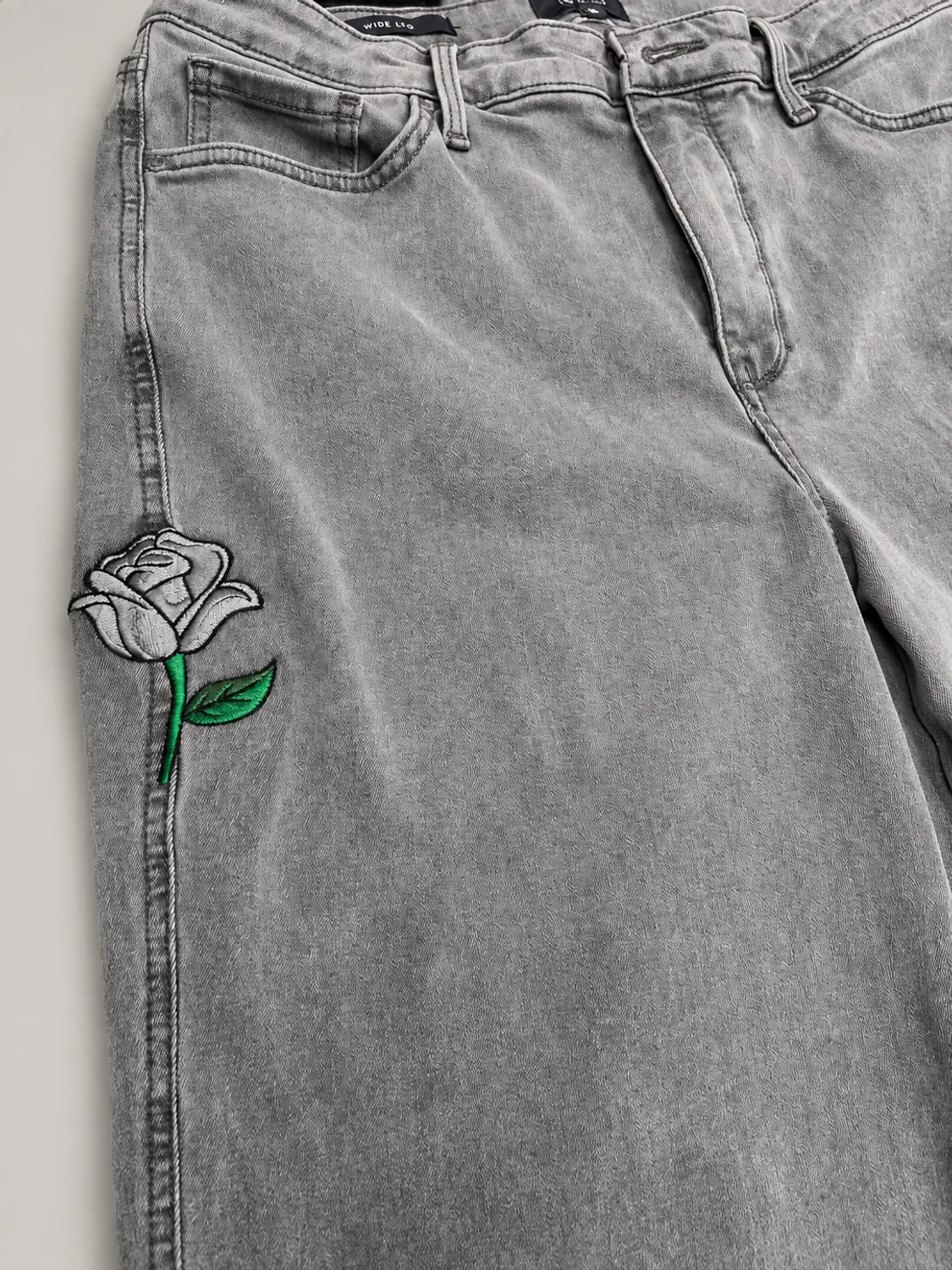 Gray jeans with a rose embroidered over a repaired hole